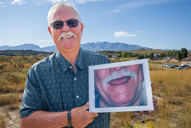 patient smiling and holding their before procedure picture outside of the dental practice